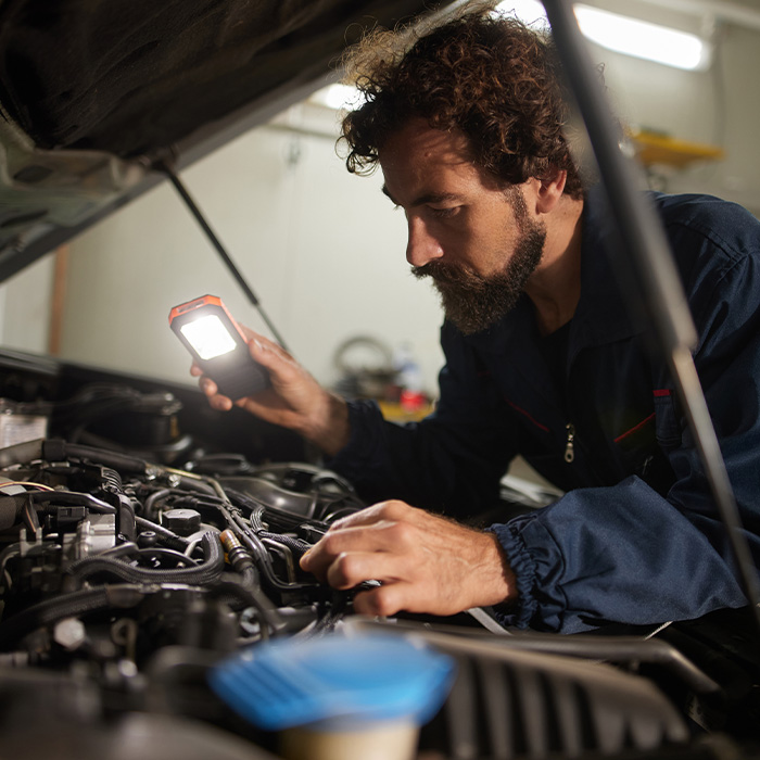 Car mechanic inspecting engine with flashlight in garage